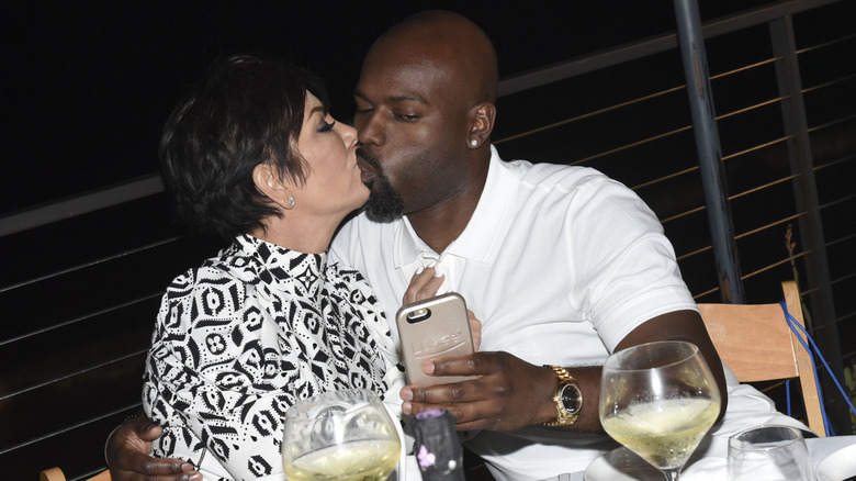 Kris Jenner and Corey Gamble kissing at a table while Gamble takes a selfie.