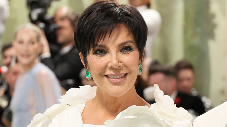Kris Jenner smiling and wearing earrings with large green gems.