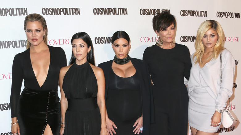 Khloé, Kourtney, and Kim Kardashian posing on step-and-repeat with Kris and Kylie Jenner