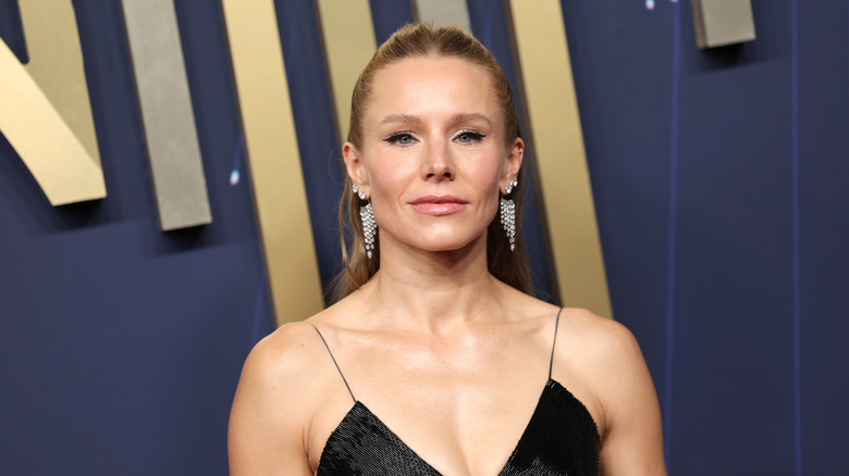 Kristen Bell smizing for the cameras on the red carpet with her hair pulled back in a half-up look