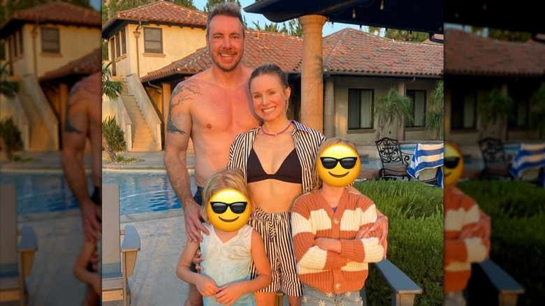 Dax Shepard, Kristen Bell, and their two daughters, whose faces are covered by smiling emoji, posing for a family photo in front of a pool.