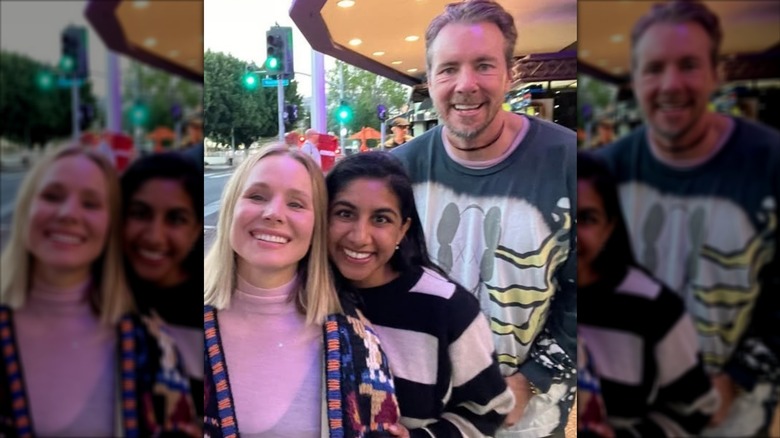 Monica Padman posing between Kristen Bell and Dax Shepard on a sidewalk with traffic lights in the background.