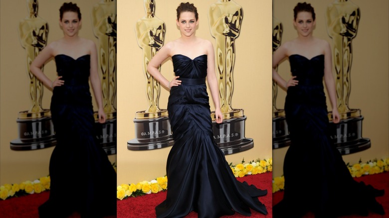 Kristen Stewart posing in a navy blue gown on an Oscars red carpet.