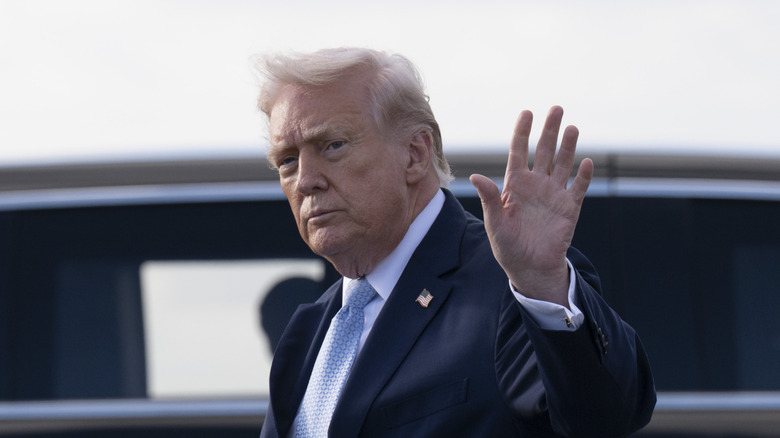 Donald Trump in a dark suit waving at cameras after stepping off Air Force One
