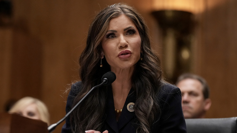 Kristi Noem speaking into a microphone while wearing a black blazer
