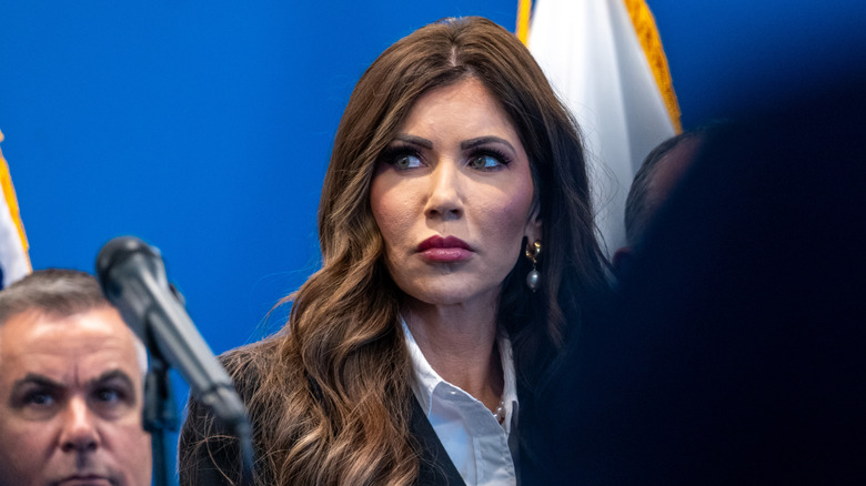 Kristi Noem behind a microphone and person, glaring off to her side.