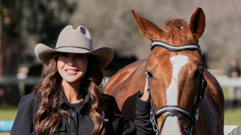 A smiling Kristi Noem wearing a cowboy hat while holding onto a horse