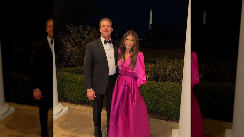 Kristi Noem smiling in a pink dress next to her husband.