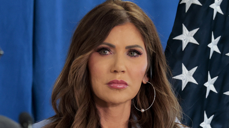 Kristi Noem straight-faced and staring off the to the side, one giant hoop earring exposed