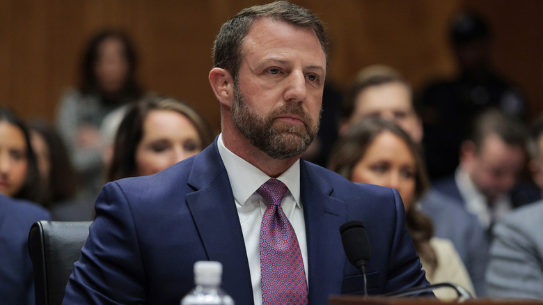 Markwayne Mullin listening during a hearing in a navy suit with a purple tie