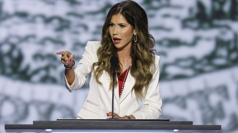 Kristi Noem behind a microphone, pointing at someone or something in front of her