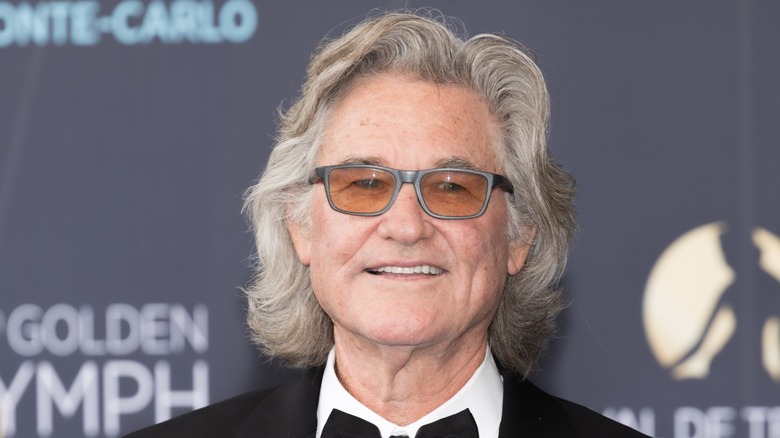 Kurt Russell smiling and posing wearing orange shades, a bow tie and suit.