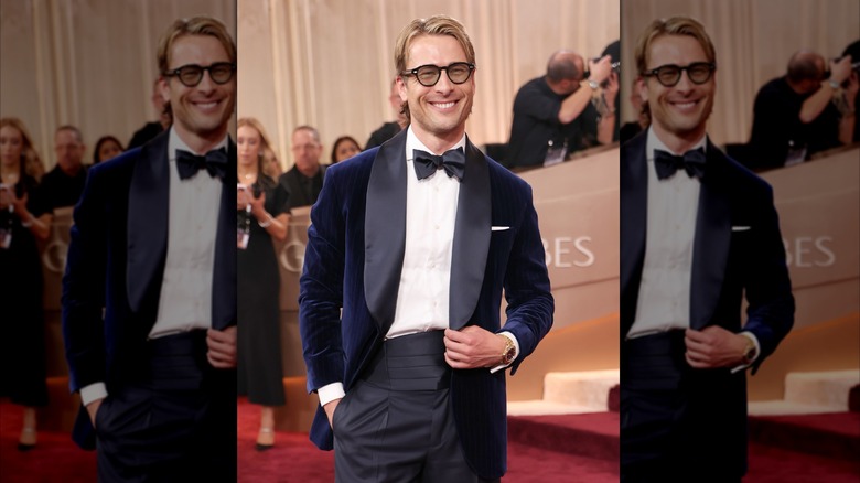 Glen Powell in a navy blue suit and glasses