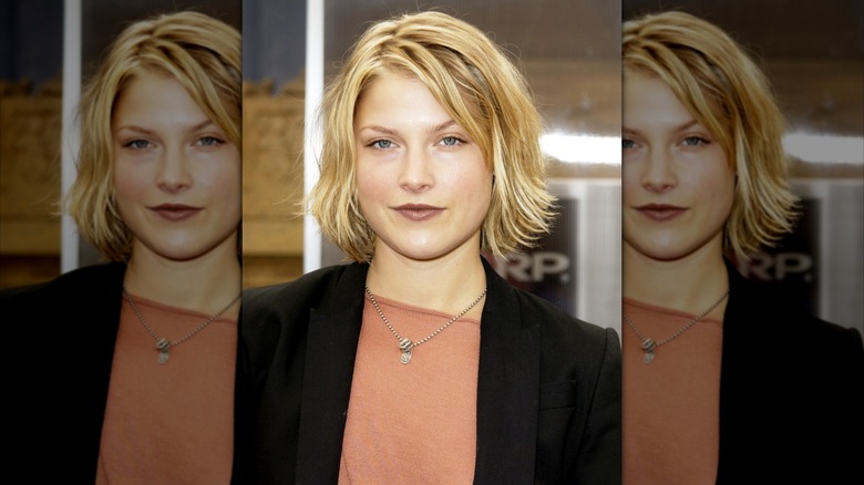 Ali Larter in 2002 with a blond mid-length bob wearing a black jacket over an orange shirt
