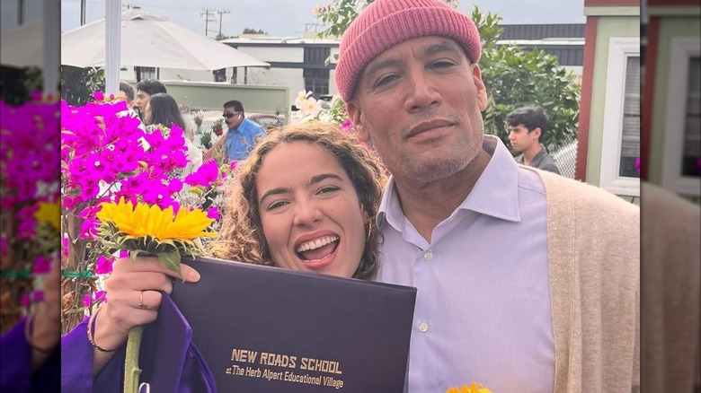 Jaya Harper holds a sunflower and her diploma while posing with her dad Ben Harper.