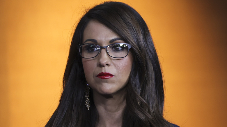 Lauren Boebert posing in front of an orange background looking glum
