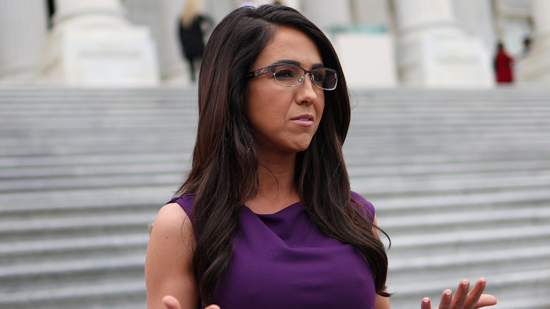 Lauren Boebert gesturing in a purple dress in front of a staircase
