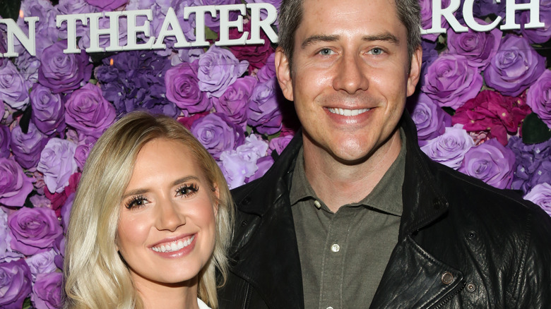 Arie Luyendyk and Lauren Burnham smile in front of rose backdrop