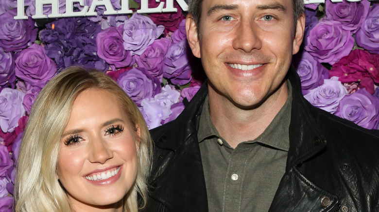 Arie Luyendyk and Lauren Burnham smile in front of rose backdrop