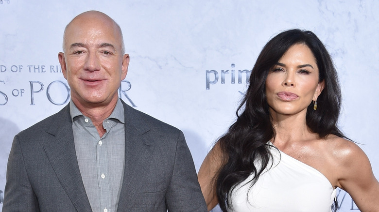 Lauren Sanchez wearing a white dress while her hand is wrapped around Jeff Bezos' arm, who's in an all-gray blazer and collared shirt.