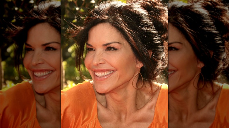 Lauren Sánchez in an orange top smiling at something off camera