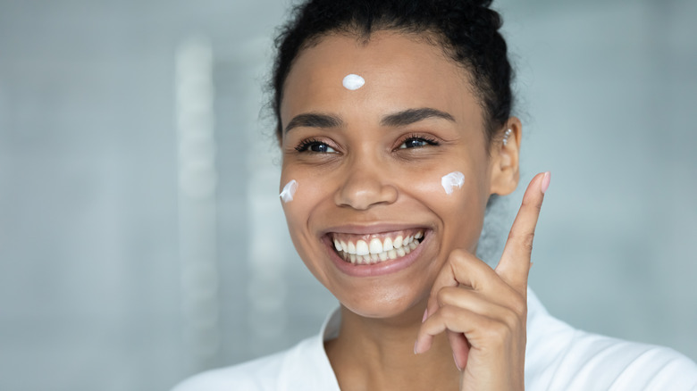 Woman smiling while applying makeup primer