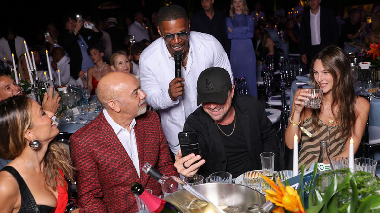 Leonardo DiCaprio talking a selfie with Vittoria Ceretti while Jamie Foxx stands behind him with a microphone