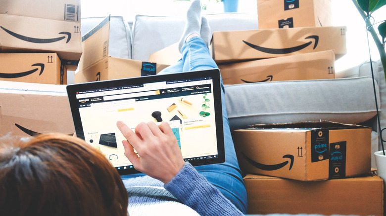 person laying in a pile of amazon prime boxes with their feet up on a couch