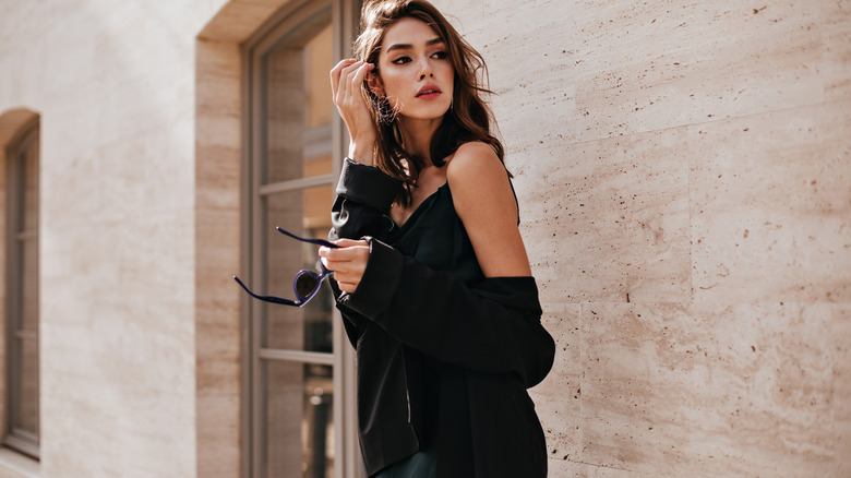 Woman wearing black dress brushes her hair behind her ear 