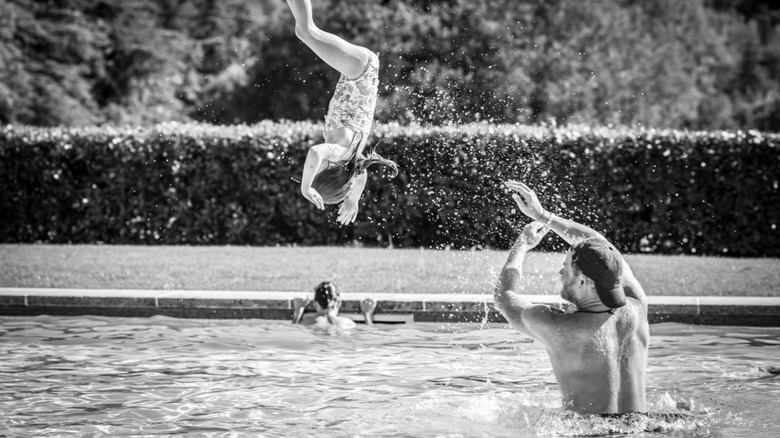 Prince Harry flipping Princess Lilibet into a pool while Prince Archie swims in the background