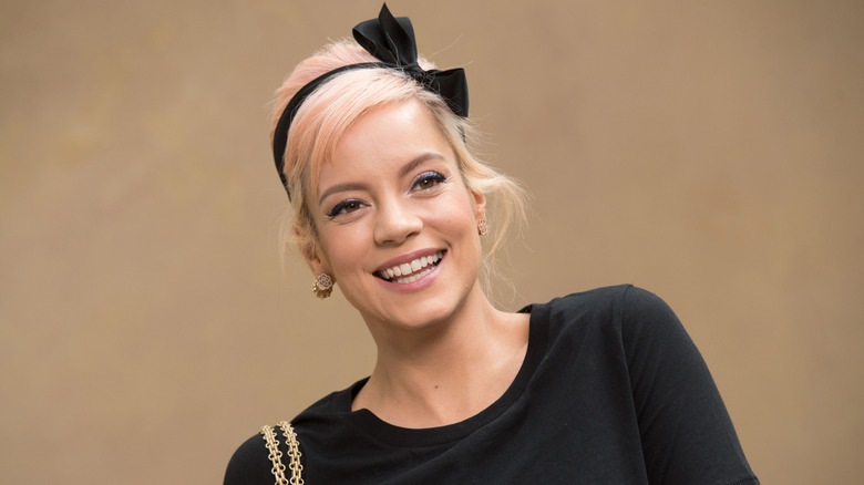 Smiling Lily Allen with light pink hair and a black headband with a bow.
