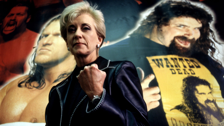 Linda McMahon posing in front of backdrop prominently featuring Triple H and Mick Foley