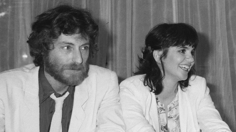 Linda Ronstadt in a white jacket smiling next to J.D. Souther at a conference in 1981.