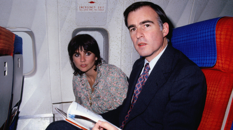 Linda Ronstadt leaning over in an airplane seat next to California Governor Jerry Brown.