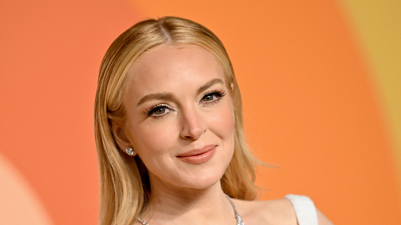 Lindsay Lohan smirking in a white dress and green necklace at the Vanity Fair Oscar party.