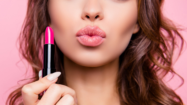Woman pursing lips while holding lipstick