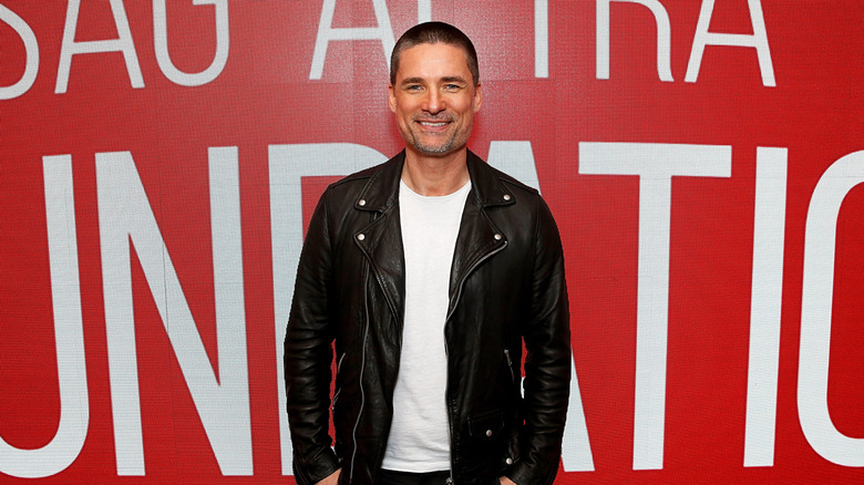 Warren Christie wearing a black leather jacket over a white shirt and jeans