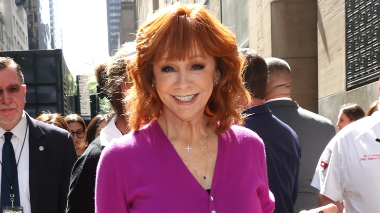 Reba McEntire smiling for photos in a black blazer and white shirt