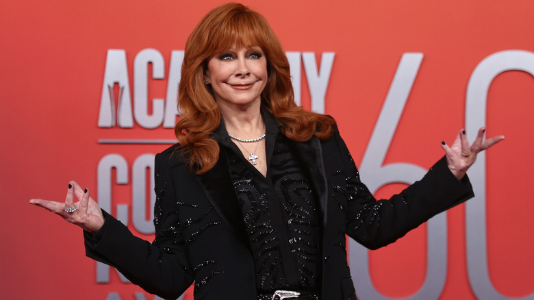 Reba McEntire posing for photos with her arms outstretched in an all-black outfit