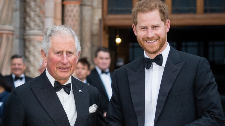King Charles III and Prince Harry smiling while posing together in tuxedos