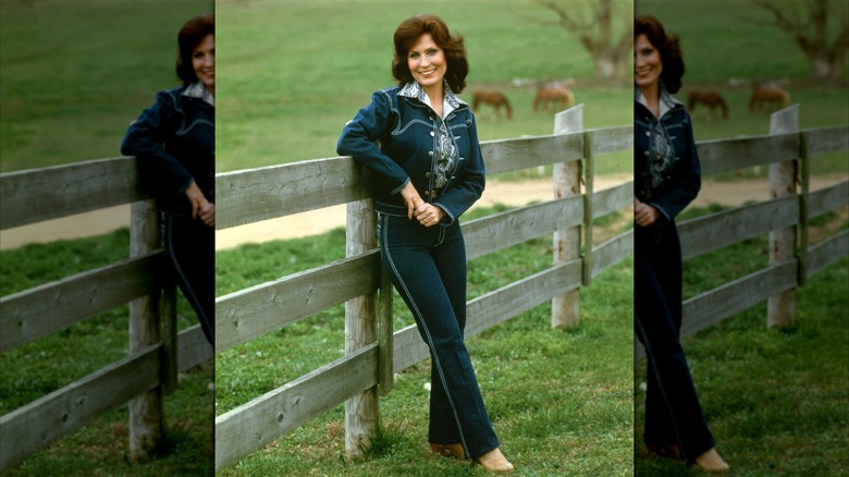 Loretta Lynn wearing a denim suit in front of cows and wooden fence