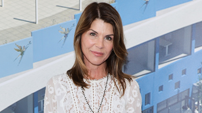 Lori Loughlin smiling while posing at an event in a white lace dress