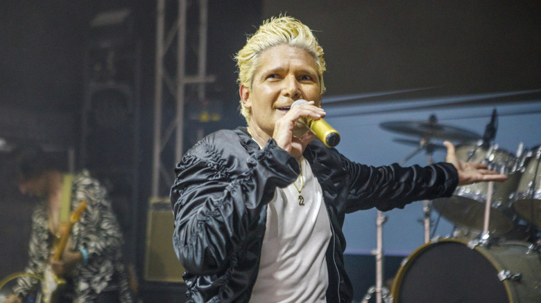Corey Feldman performing onstage with a gold microphone in a black jacket and white shirt