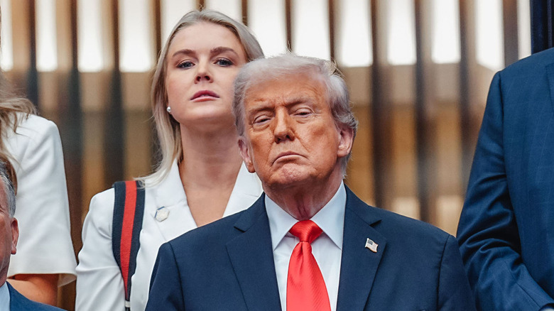 Karoline Leavitt standing behind Donald Trump while both look annoyed