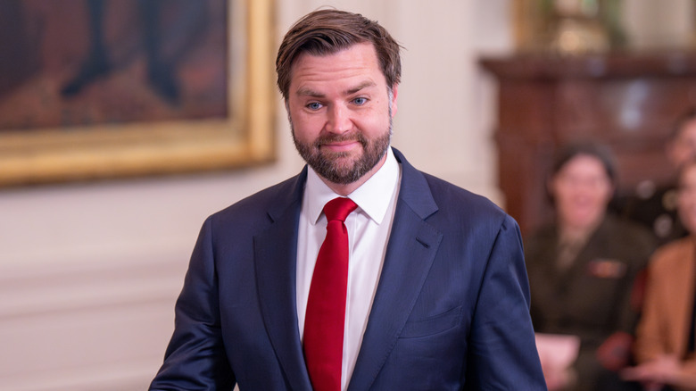 JD Vance smiling in a blue suit with a red tie