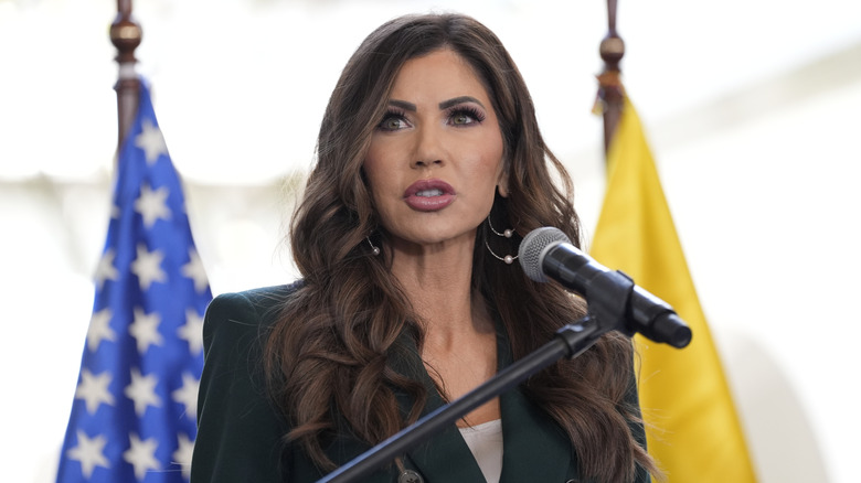 Kristi Noem giving a speech in a black blazer with a white top underneath