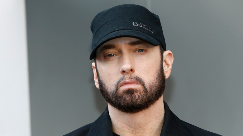 Eminem in a black cap and outfit with a bearded look
