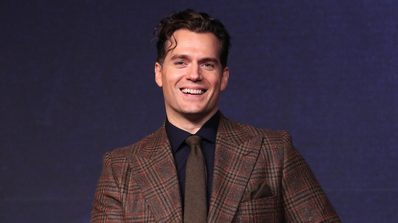 Henry Cavill smiling in a brown plaid suit
