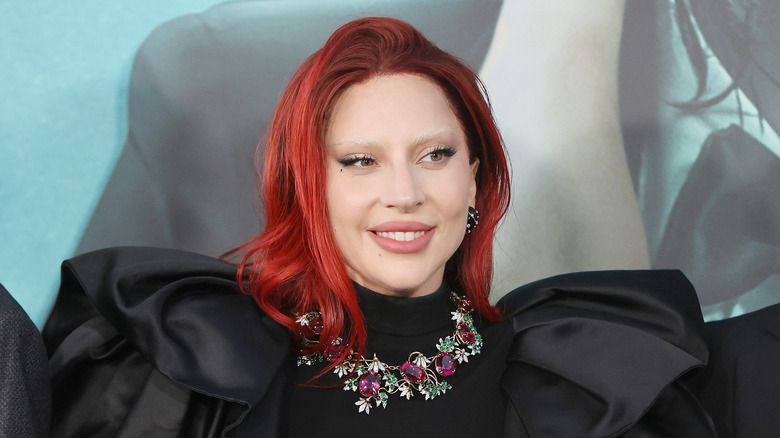 Lady Gaga with red hair and bleached brows in a dramatic black dress
