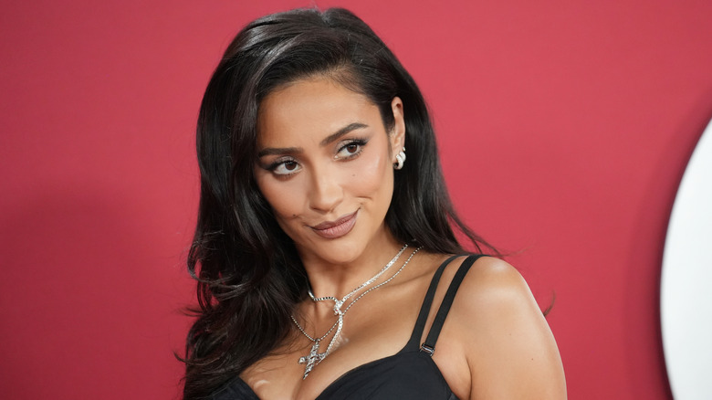 Shay Mitchell in a strappy black dress against red backdrop